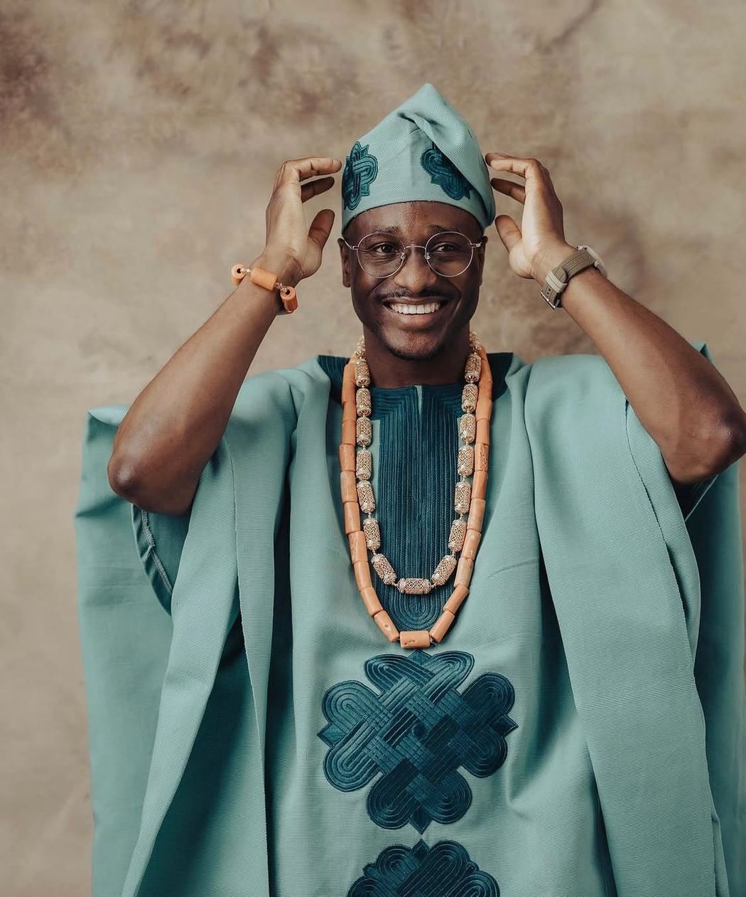 A smiling groom in a sage TAB agbada with coral beads and a matching fila